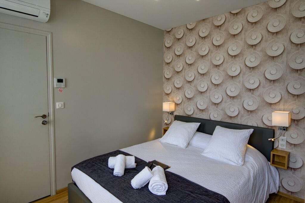 A neatly made bed with white linens and rolled towels, a wall with a circular pattern, and bedside lamps.