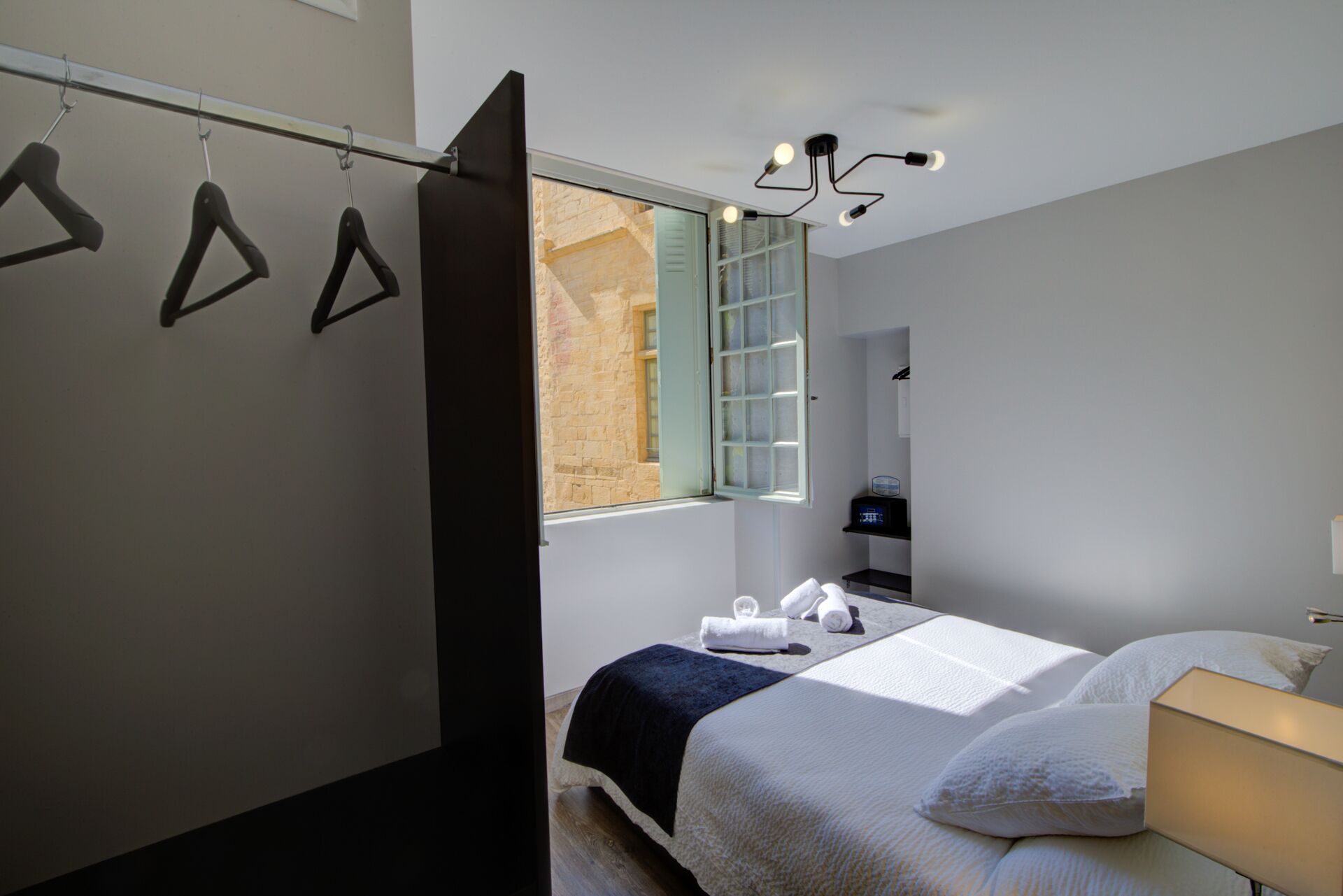 Une chambre à coucher moderne, avec un lit, une table de chevet, une lampe et une fenêtre donnant sur un immeuble en briques.
