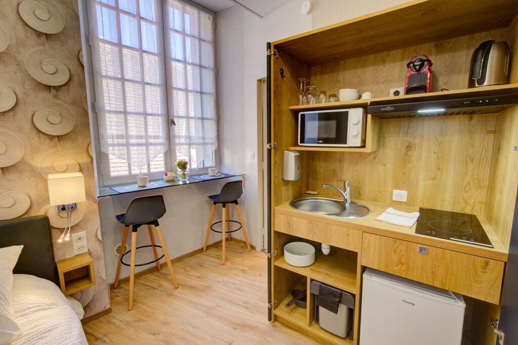 Une petite pièce comprenant un lit, un bureau, deux chaises, une fenêtre, un four à micro-ondes, un évier et un réfrigérateur.