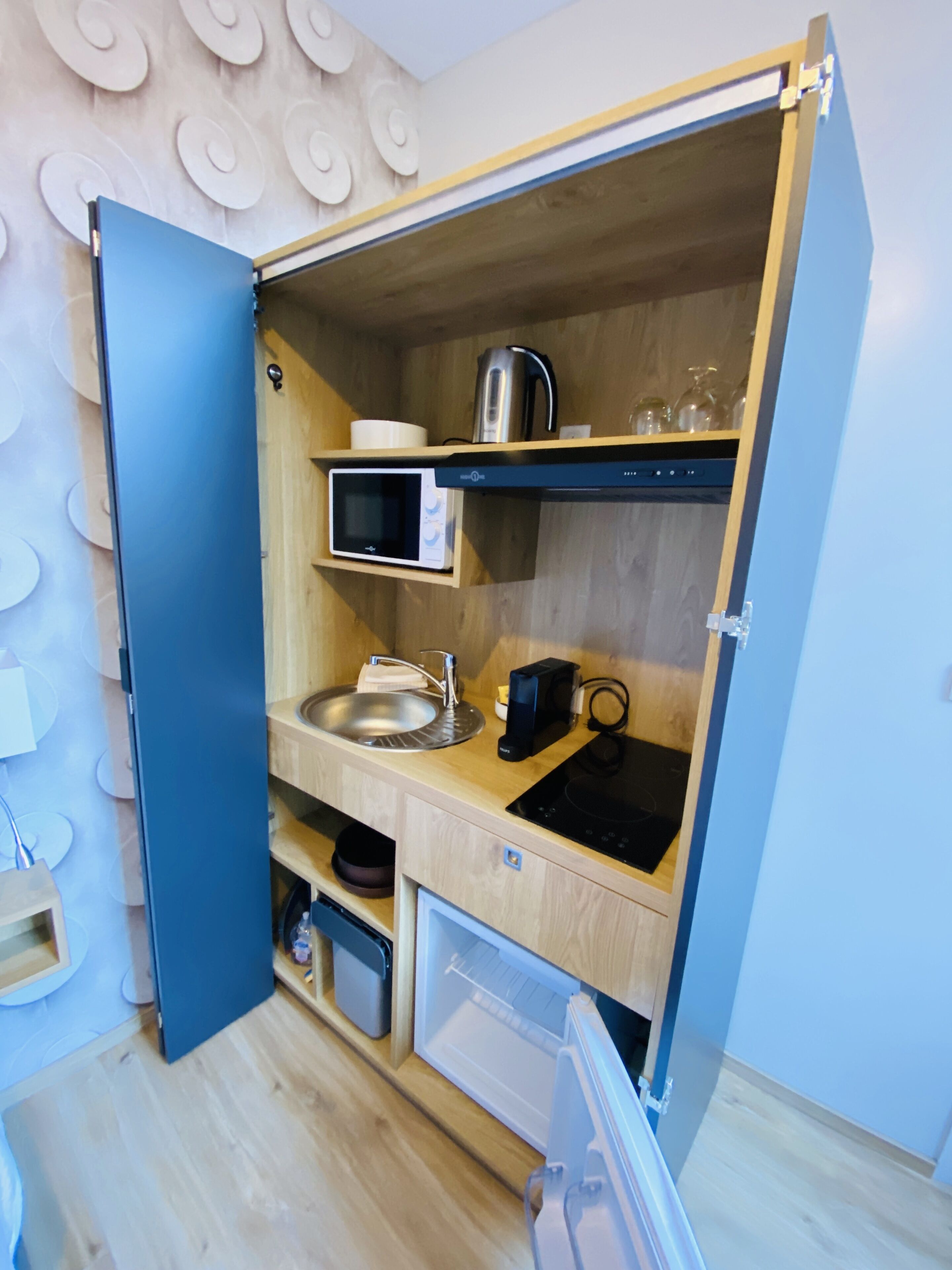 A compact kitchen with a microwave, sink, kettle, and a small refrigerator.