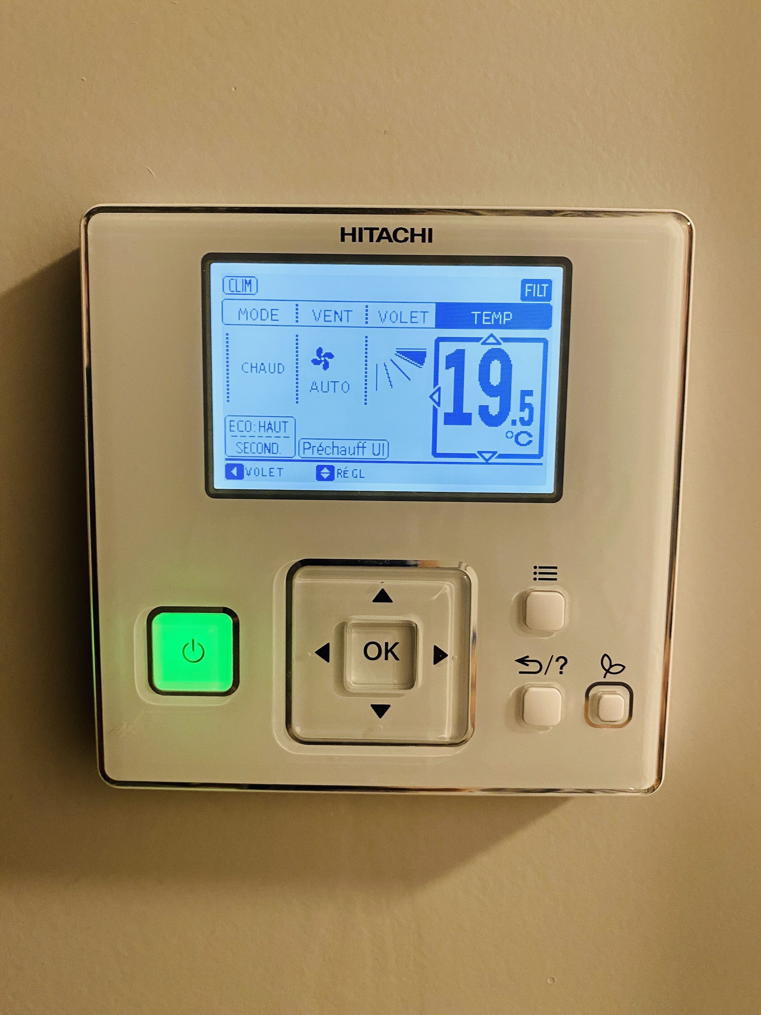 A HITACHI thermostat with a digital display showing 19.5°C, a green power button, and several control buttons including an OK button and directional arrows.
