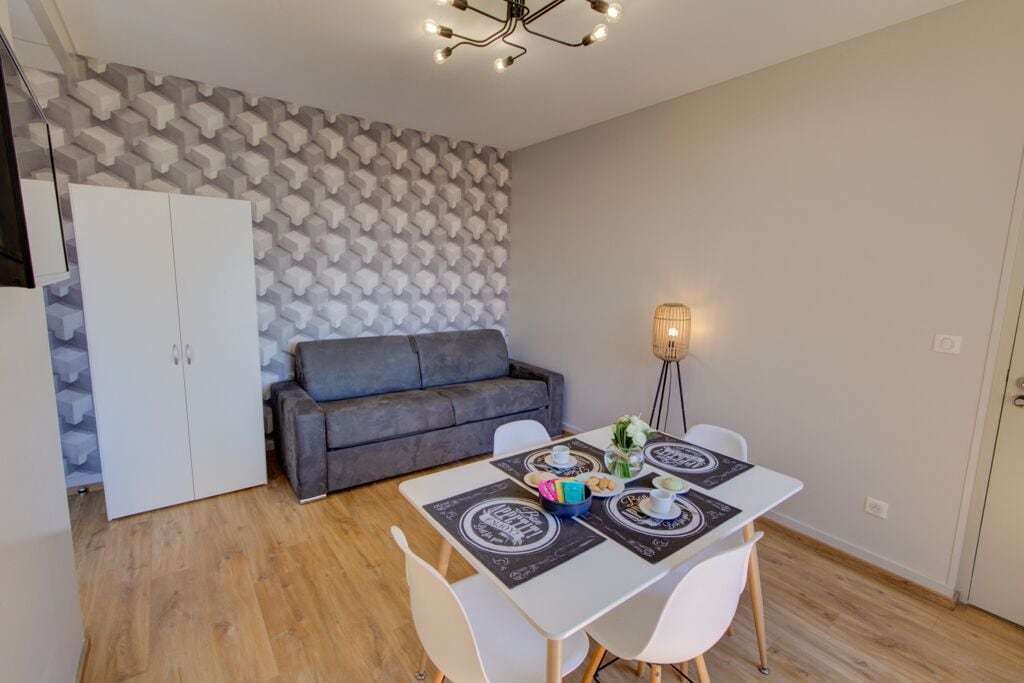 Una sala de estar moderna con un sofá gris, armarios blancos y una mesa de comedor con individuales y una vela.