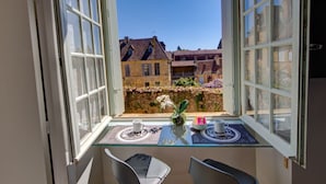 Een balkon met een glazen tafel, twee stoelen en uitzicht op traditionele gebouwen.