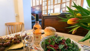 A dining table with a bottle of wine, a glass, a loaf of bread, a bowl of greens, and a bunch of grapes. - Capel Bach  -  a near a pub that sleeps 6 guests  in 3 bedrooms (Llanystumdwy)