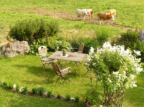 Ein Garten mit Holztisch und -stühlen, umgeben von viel Grün und Blumen.