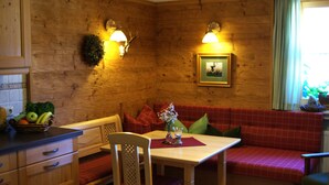 Ein Holzblockhaus-Innenraum mit Esstisch, Bankbestuhlung und einem an der Wand hängenden Bild.