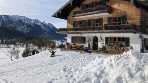 Eine Holzchalet mit Balkon, verschneiter Landschaft und Bergen im Hintergrund.