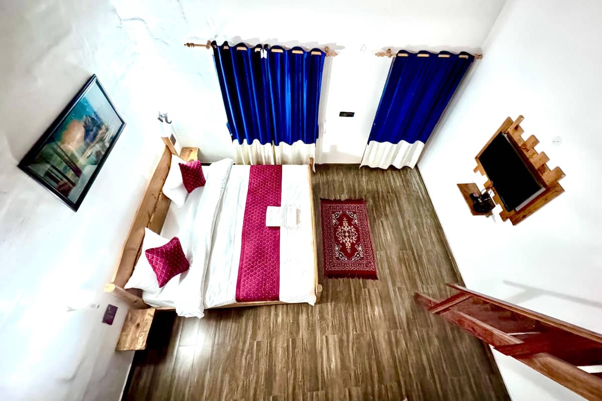 A room with a bed, a wooden bench, a red patterned rug, and blue curtains.
