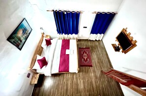 Una habitación con una cama, un banco de madera, un tapete rojo estampado y cortinas azules.
