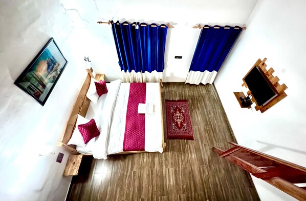 A room with a bed, a wooden bench, a red patterned rug, and blue curtains. - The Farm Cottages (Nainital)