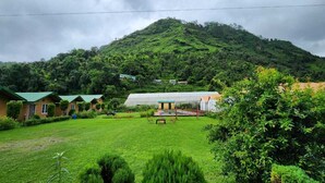 A lush green landscape with a hill in the background, a greenhouse, and several small buildings with green roofs. - The Farm Cottages (Nainital)