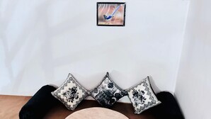 A round, blue and beige cushioned seating area with black and white patterned pillows against a white wall. - The Farm Cottages (Nainital)