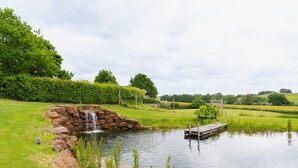 A pond with a wooden dock, surrounded by lush greenery and a stone waterfall.