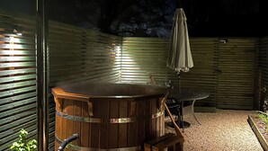 A hot tub with a wooden bench, a table with an umbrella, and a metal pole.