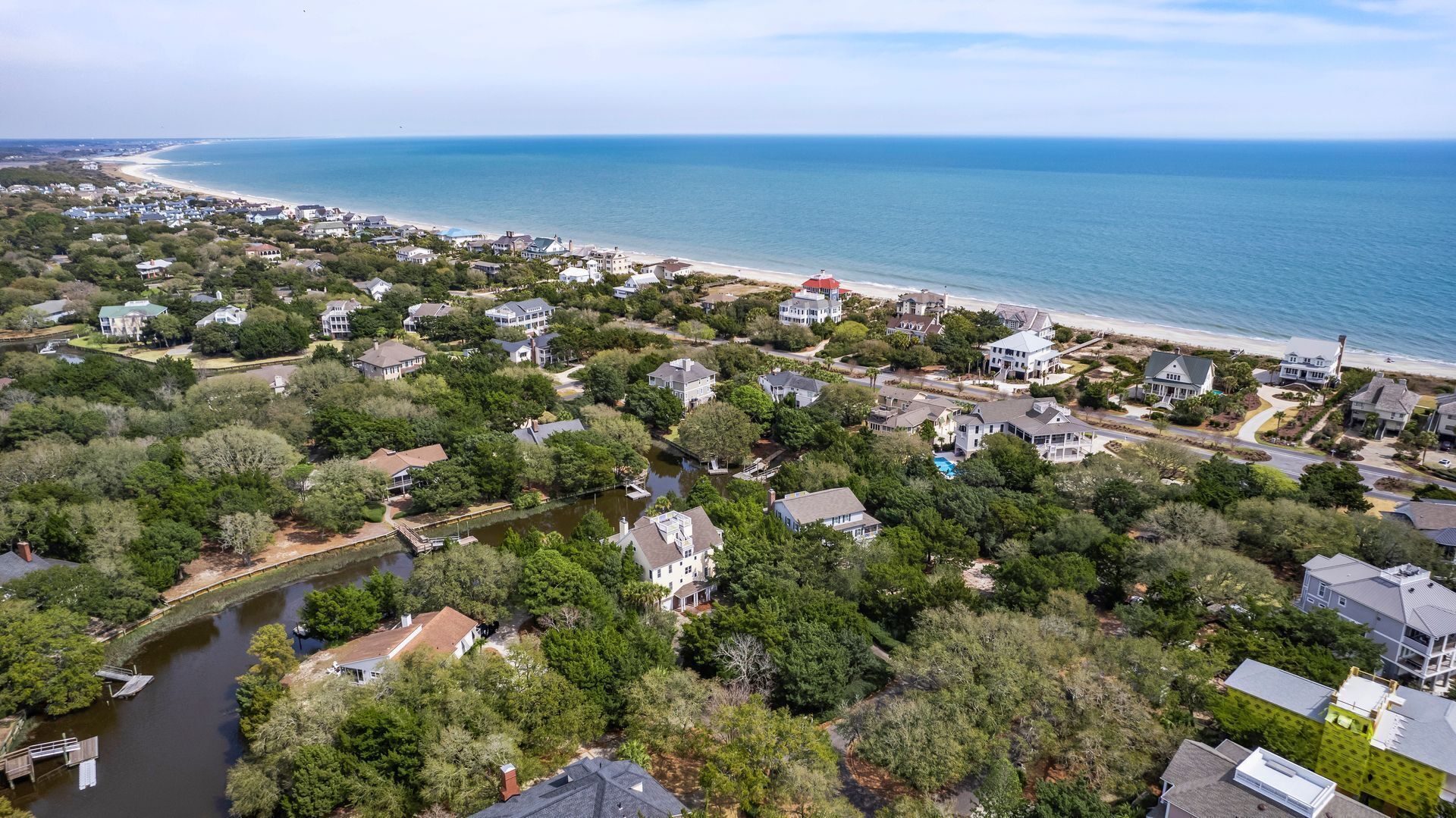 An aerial view of a coastal residential area with houses, a river, and a beach.