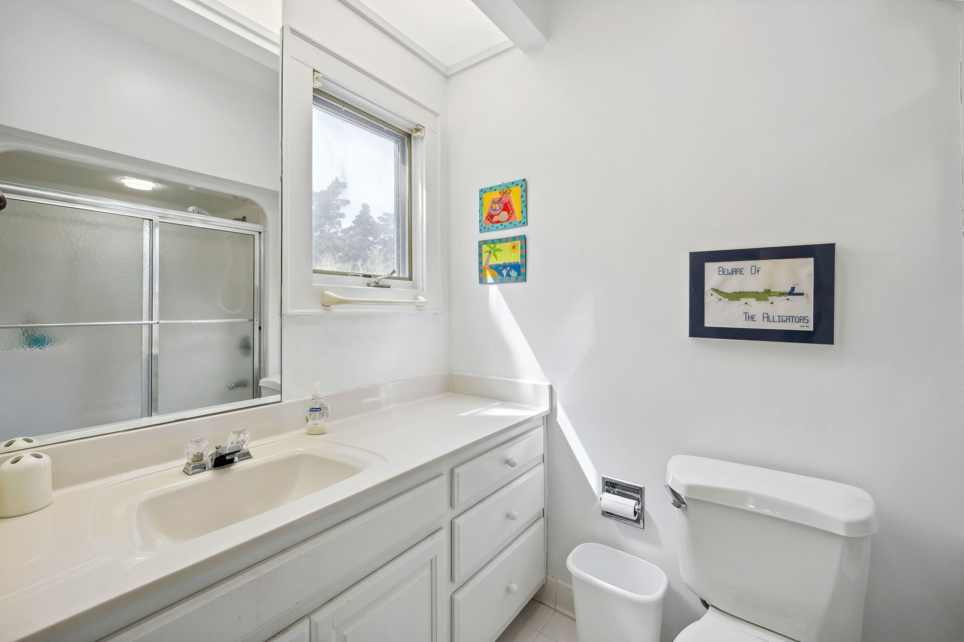 Ein Badezimmer mit Waschbecken, Spiegel und Toilette. An den Wänden hängen zwei Bilder in Rahmen.