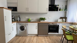 A modern kitchen with a washing machine, dishwasher, oven, and a dining area with a table and chairs.