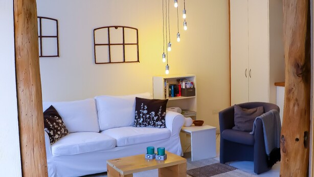 A living room with a white sofa, a wooden coffee table, a bookshelf, and a grey armchair.