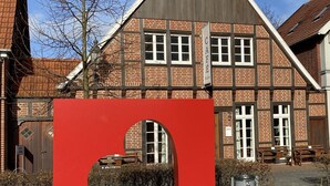 A red sign with "SEPPENRADE Liebe" in front of a traditional brick building with multiple windows and a sloped roof.