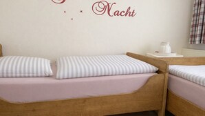 A bedroom with two wooden beds, each with a pillow and a bedside table with a white pitcher.