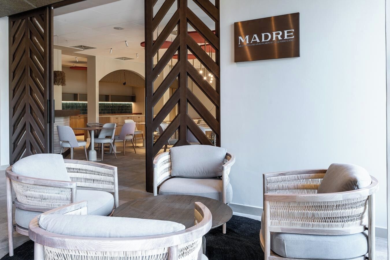 A modern lounge area with wicker furniture and a sign reading "MADRE".