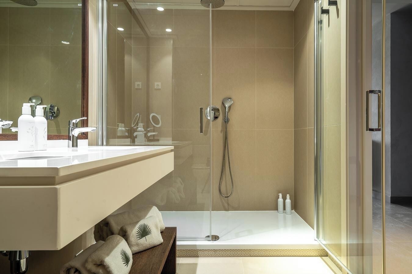 A modern bathroom with a glass-enclosed shower, a vanity with a mirror, and a bench with towels.