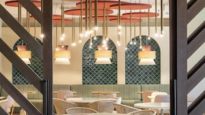 Interior de restaurante con mobiliario de mimbre, lámparas colgantes y paredes con diseño verde.