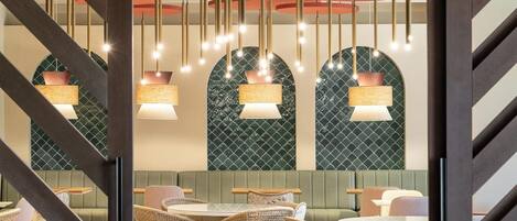 A restaurant interior with wicker furniture, hanging pendant lights, and green patterned walls.