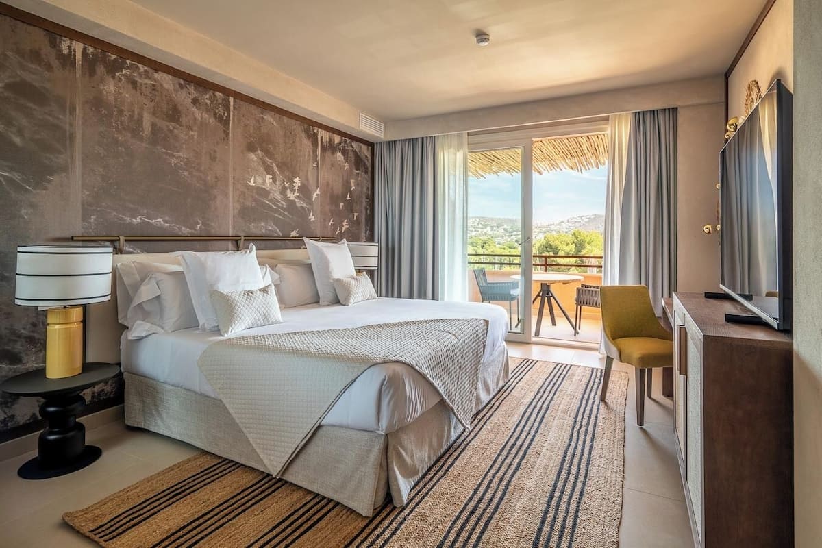 Ein Hotelzimmer mit einem großen Bett, einem Schreibtisch mit Fernseher und einem Balkon mit Blick.