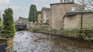A river flowing through a historic town with stone buildings and a bridge. - Bear Pit Cottage (High Peak)