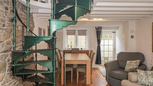 A spiral staircase with a stone wall, a wooden dining table, and a grey sofa in a well-lit room. - Bear Pit Cottage (High Peak)