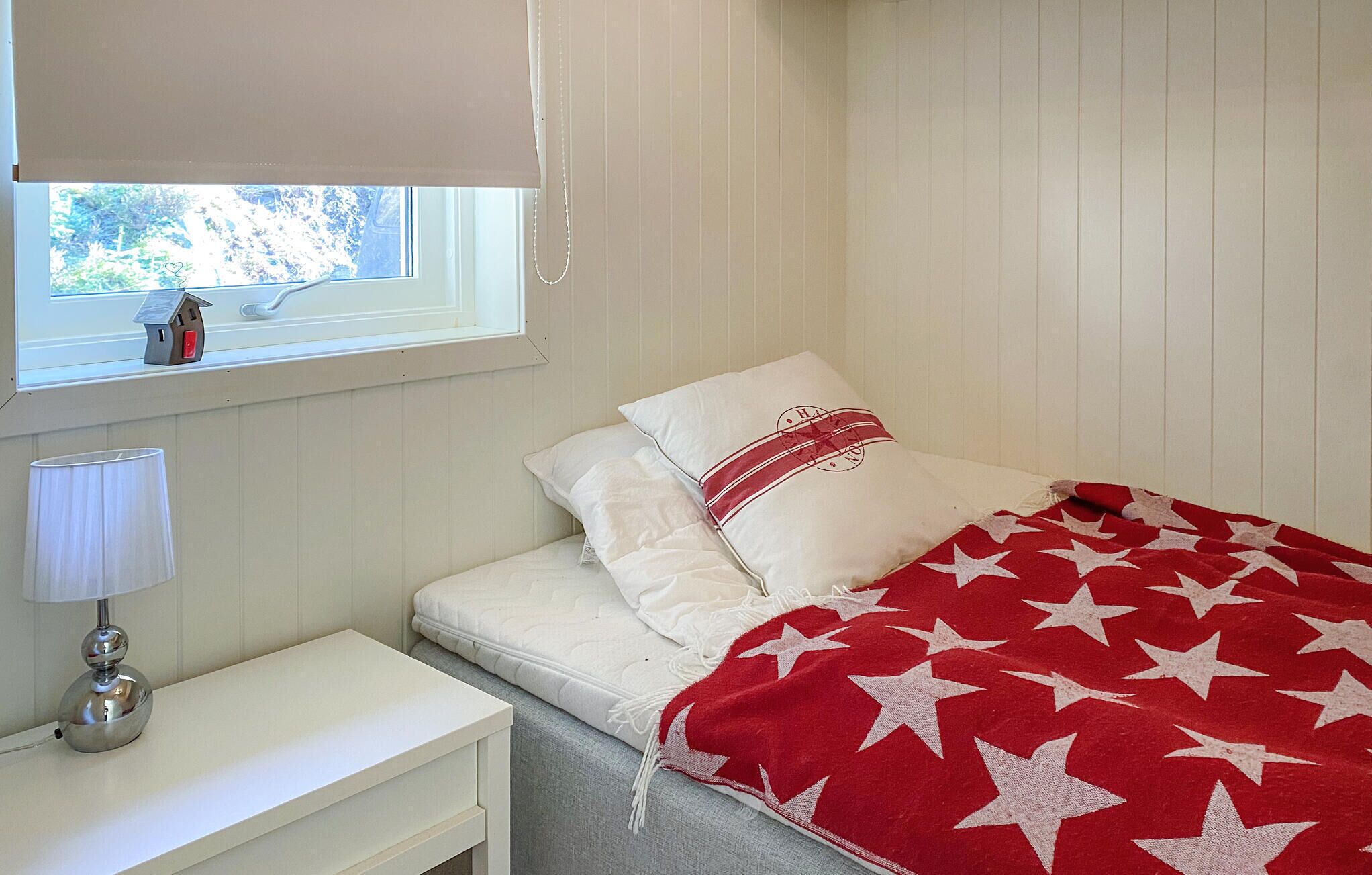 Une chambre à coucher avec un lit, une table de chevet, une lampe et une fenêtre donnant sur des arbres.