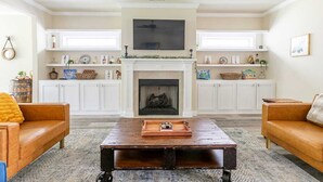 Een woonkamer met een open haard, twee banken, een salontafel en planken met decoratieve objecten.