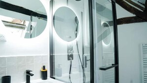 Ein modernes Badezimmer mit Duschkabine aus Glas, einem runden Spiegel und einem weißen Waschbecken mit schwarzem Wasserhahn.