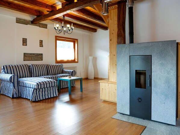 A cozy living room with a striped sofa, a small table, and a modern fireplace. - Stunning private villa for 4 people with WIFI and TV (Ovaro)