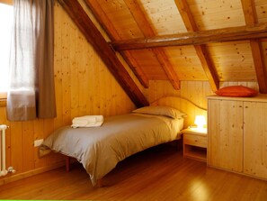 A cozy attic bedroom with a wooden ceiling, a bed with a beige bedspread, a nightstand with a lamp, and a wooden cabinet. - Stunning private villa for 4 people with WIFI and TV (Ovaro)