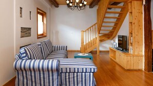 A cozy living room with a wooden staircase, a striped sofa, and a television on a wooden shelf. - Stunning private villa for 4 people with WIFI and TV (Ovaro)
