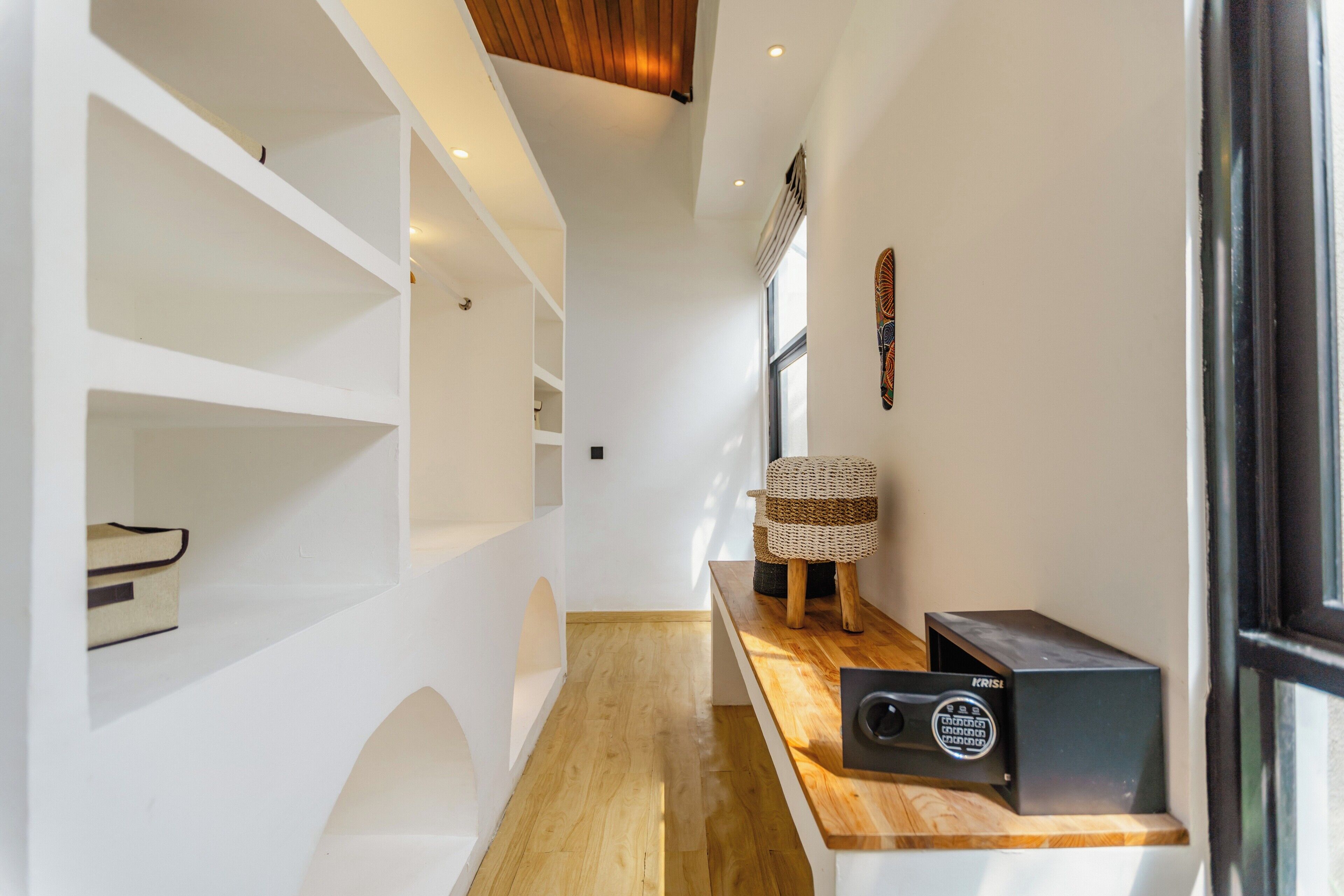 Un pasillo estrecho con estanterías blancas, una cesta tejida sobre una mesa de madera y un dispositivo electrónico negro sobre la mesa.