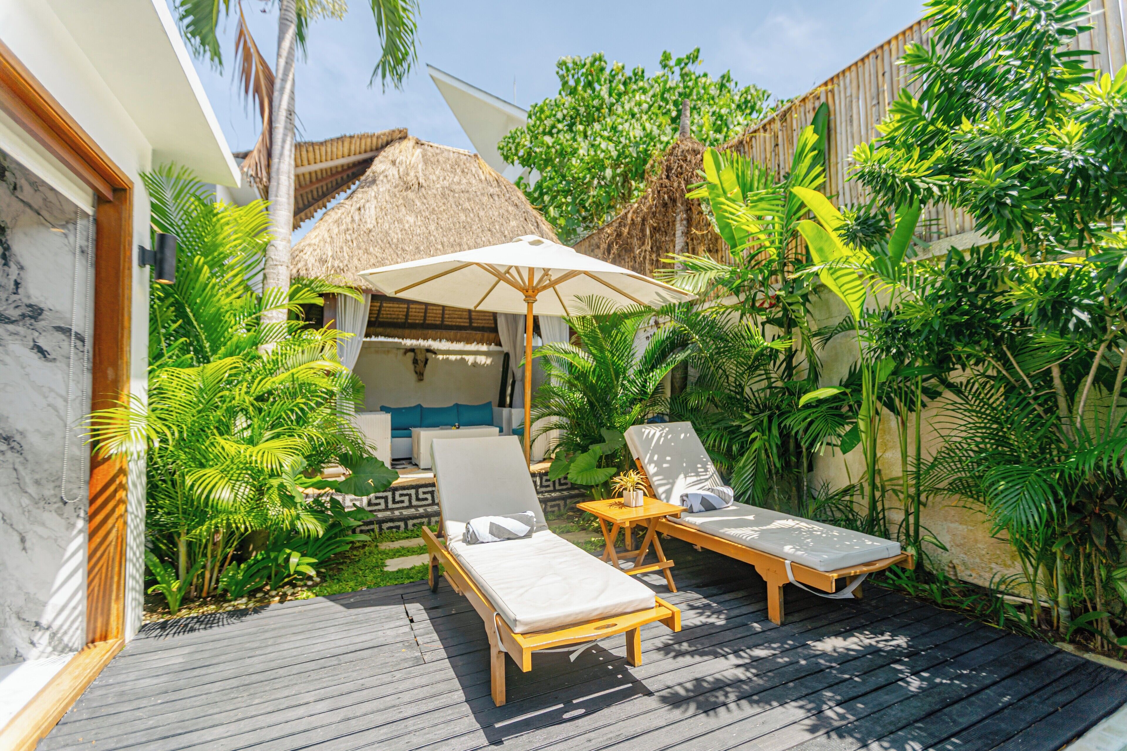 A wooden deck with two lounge chairs and a thatched-roof structure.