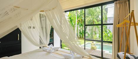 A bedroom with a canopy bed, a wooden ceiling, and a view of a swimming pool and greenery.