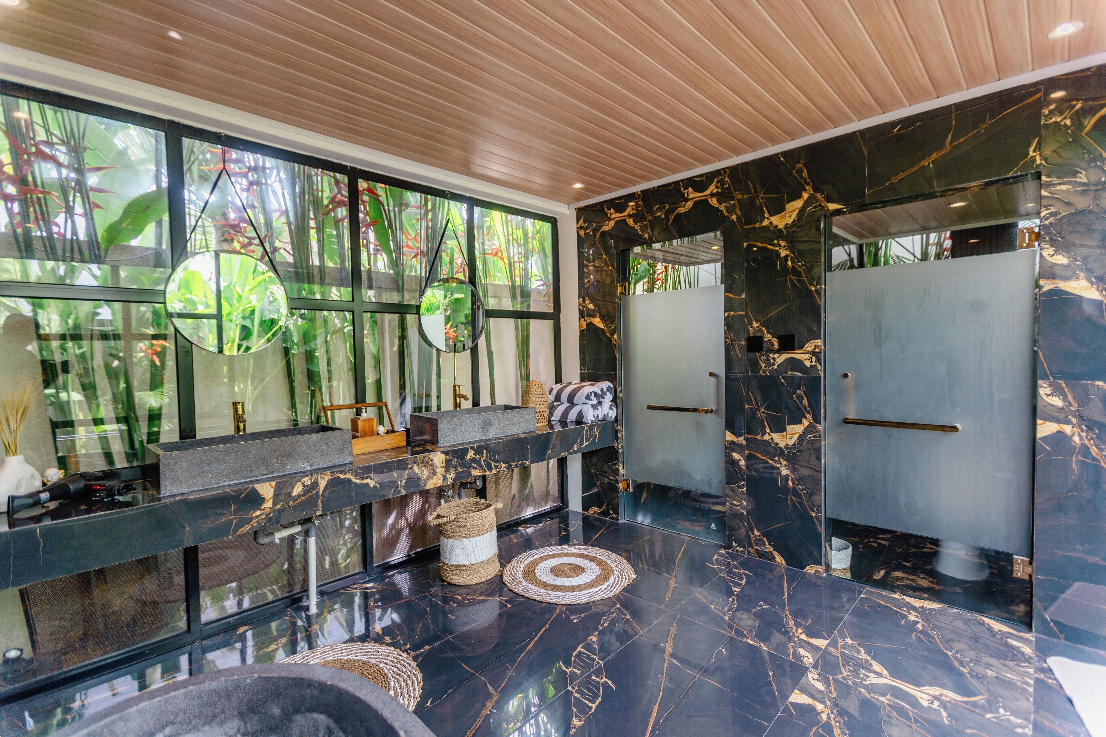 A modern bathroom with a black marble vanity, a large mirror, and a window with a view of greenery.