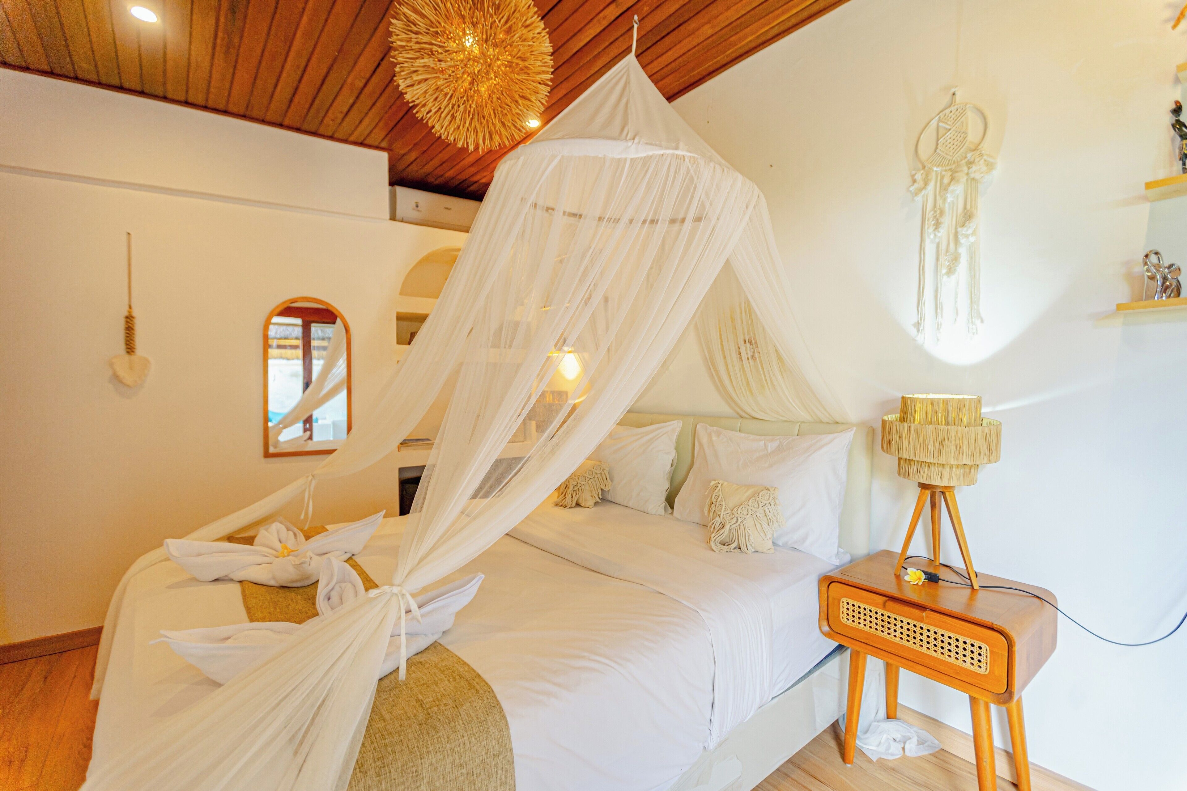 A bedroom with a canopy bed, a bedside lamp, and a dreamcatcher on the wall.
