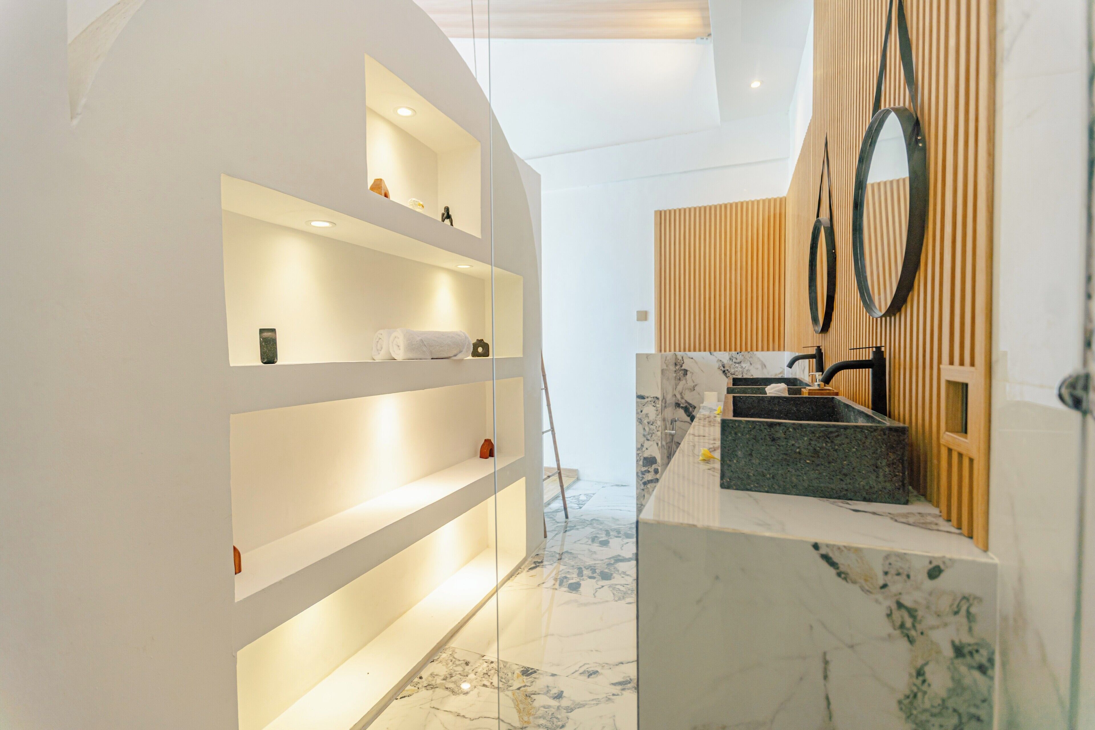 A modern bathroom with a marble sink, wooden paneling, and built-in shelves.