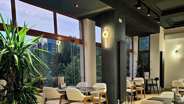 Un restaurant moderne doté de grandes fenêtres, d’un plancher en bois et d’un mélange de chaises blanches et en bois.