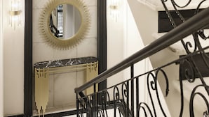 Un intérieur moderne agrémenté d’une console en marbre, d’un miroir en forme de soleil et d’un escalier avec des rampes noires décorées.