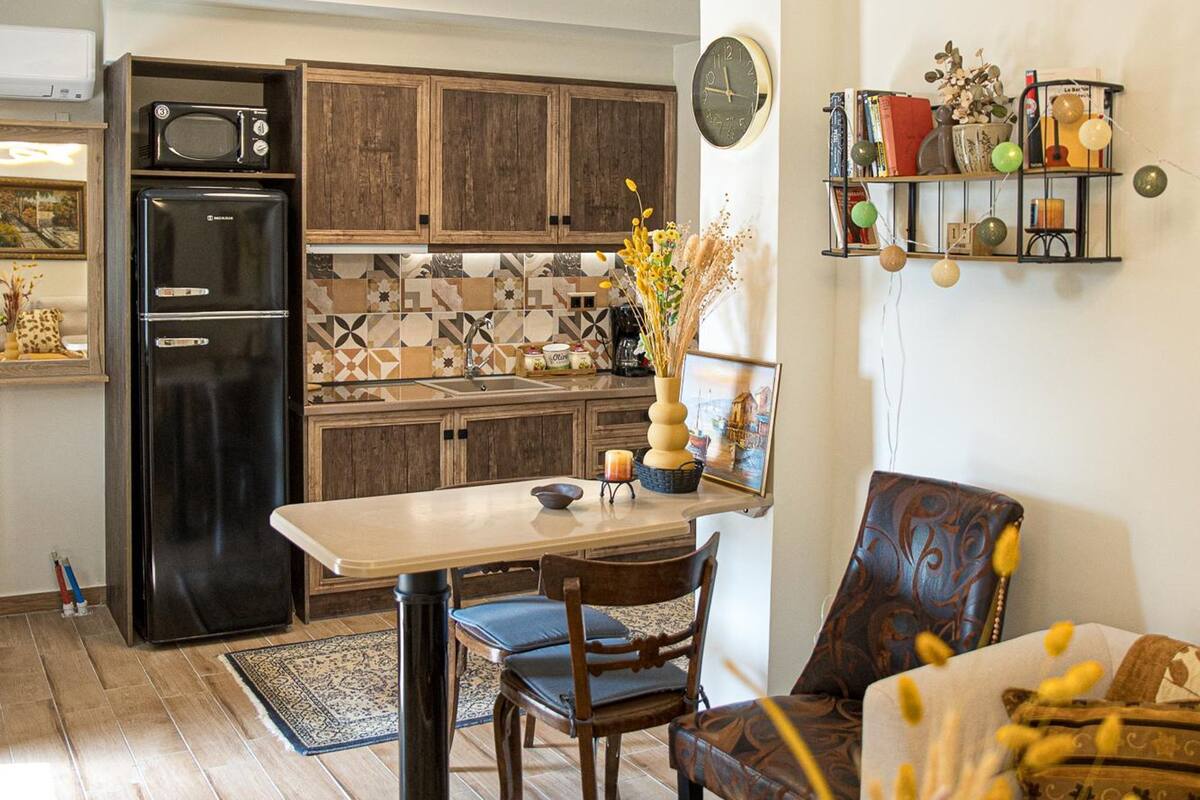 A modern kitchen with wooden cabinets, a black refrigerator, a dining table with chairs, and a pendant light.