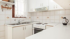 A kitchen with white cabinets, a stove, a sink, and a window with lace curtains.