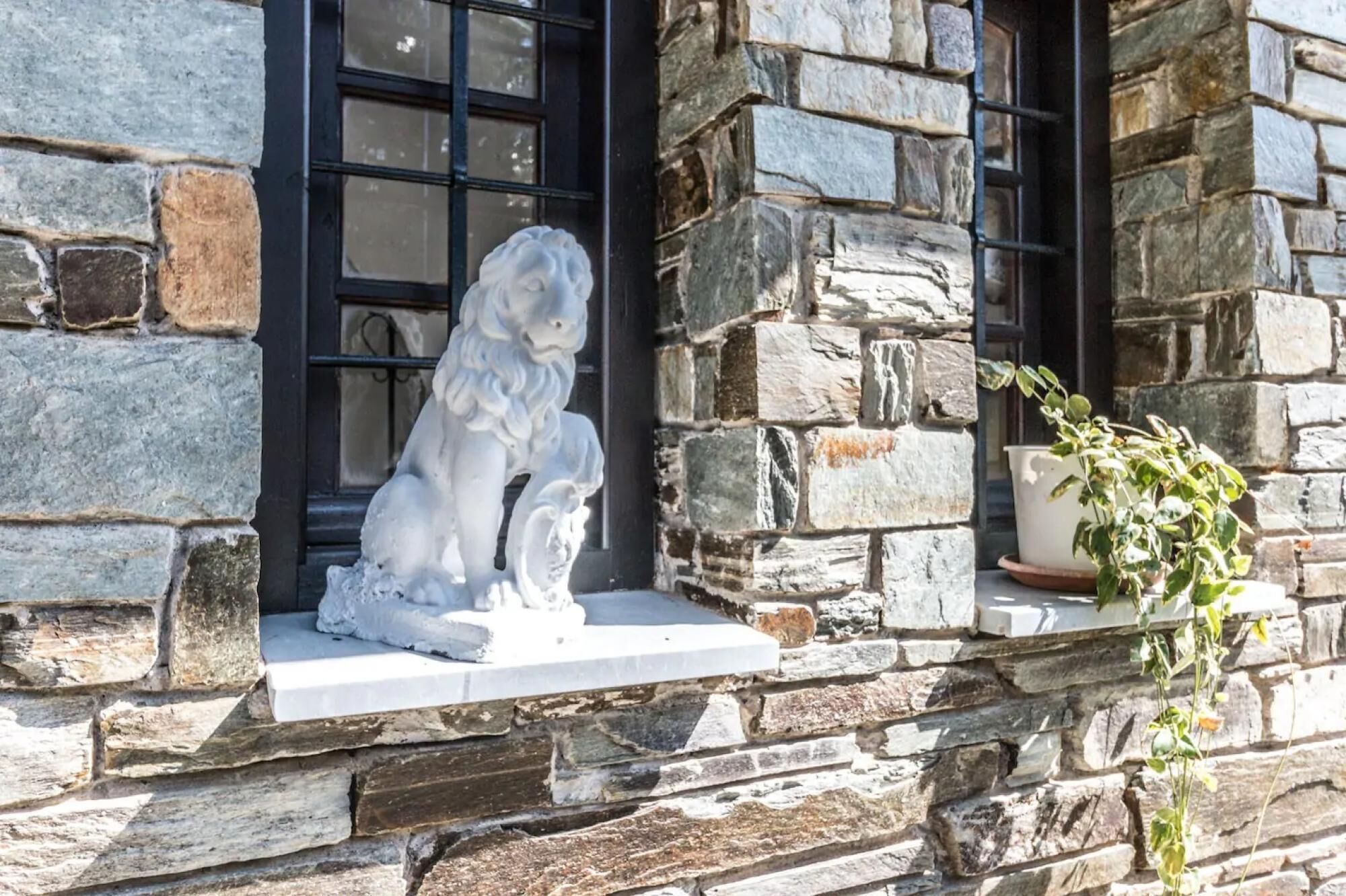 A stone building with a lion statue on the ledge, a window with black frames, and a potted plant on the right.