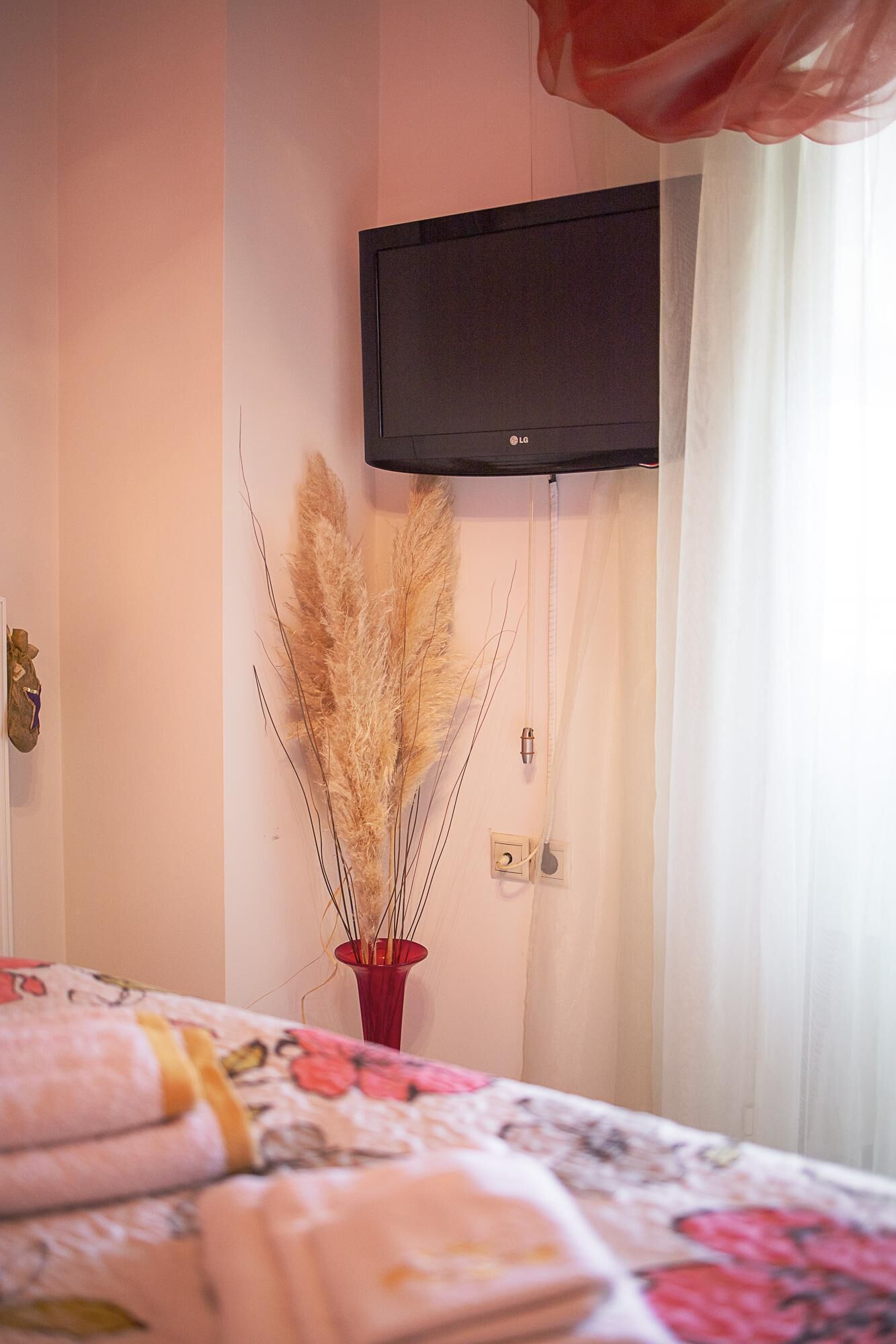A bedroom with a bed, a wall-mounted TV, and a vase with dried plants.