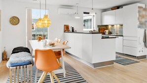 Eine moderne Küche mit weißen Schränken, einem Essbereich mit Holztisch und orangefarbenen Stühlen sowie einer Kücheninsel mit Spüle und Arbeitsplatte.